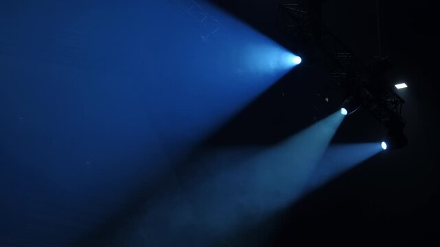 Blue spotlights illuminating a dark stage during a live concert performance