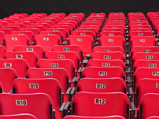 Fototapeta premium Rows of empty red stadium seats with numbered labels, repetitive pattern and perspective, sports venue interior with strong visual symmetry and structure.