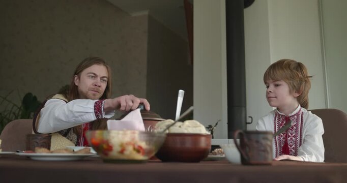 Man With Kid Boy Eat Food Lunch Dinner. Family in Ukrainian Traditional Attire Childhood. 4K 10-bit