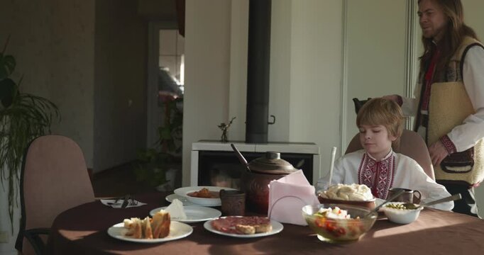 Man With Kid Boy Eat Food Lunch Dinner. Family in Ukrainian Traditional Attire Childhood. 4K 10-bit