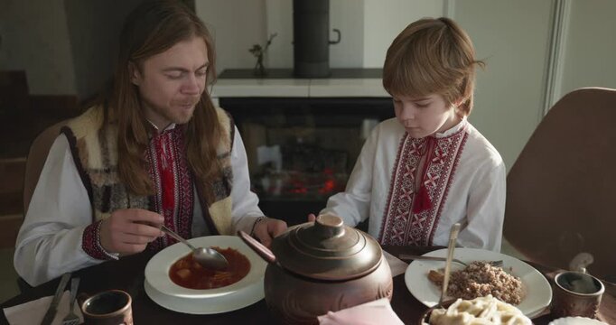 Man With Kid Boy Eat Food Lunch Dinner. Family in Ukrainian Traditional Attire Childhood. 4K 10-bit