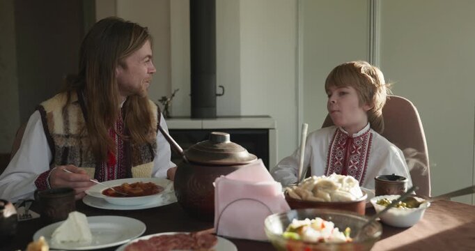 Man With Kid Boy Eat Food Lunch Dinner. Family in Ukrainian Traditional Attire Childhood. 4K 10-bit