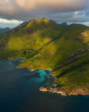Aerial view of the turquoise waters of Anse Major bay and lush green mountain peaks during golden hour in Port Glaud, Seychelles.