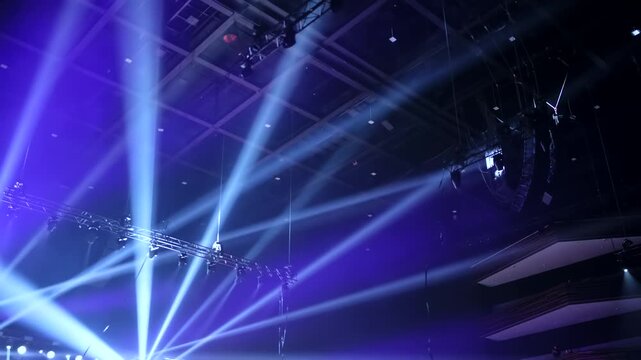 Stage lighting beams crisscrossing, illuminating a large venue for a concert event