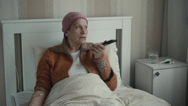 Elderly woman seriously ill lying at home with IV drip talking on phone