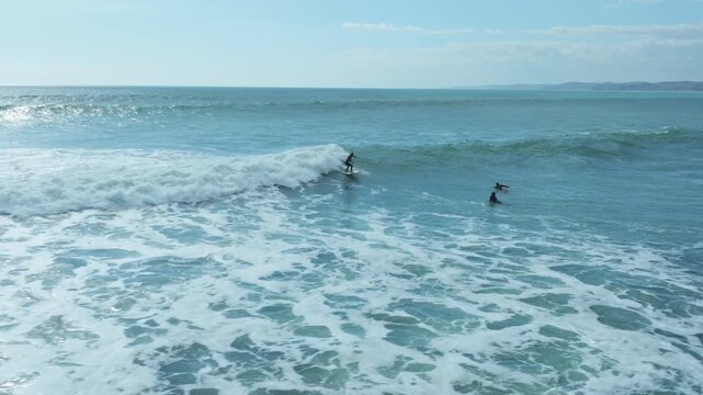 Surfers paddle in the turquoise waters off the coast of Raglan, New Zealand, enjoying the waves on a sunny day.