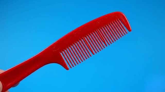 A clean 3D graphic illustration showcasing a simple red plastic hair comb levitating at an angle over a vibrant blue backdrop. Ideal for hair salon branding, personal grooming product packaging, and b
