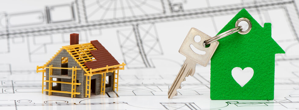 Ein Wohnungsschl&uuml;ssel mit Anh&auml;nger steht zusammen mit einem Modellhaus auf einem Bauplan,