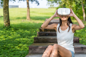 Fototapeta premium Young woman enjoying vr experience sitting in green park