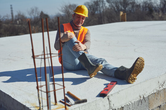 Construction worker having a accident and injured knee and leg on a construction site outdoors.