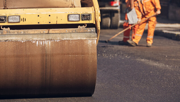 Construction workers working on a new asphalt layer on a public street.