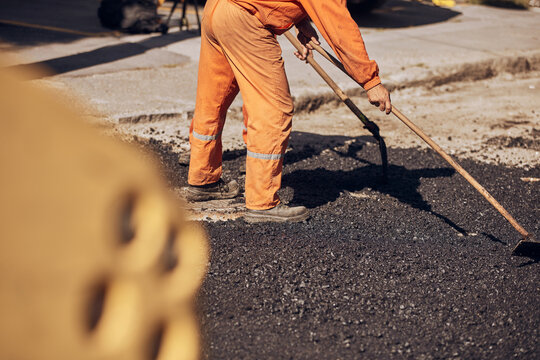 Construction worker working on a new asphalt layer on a public street.