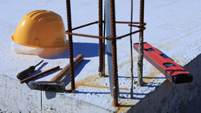 Construction tools and helmet on a cement foundation with iron rebar.