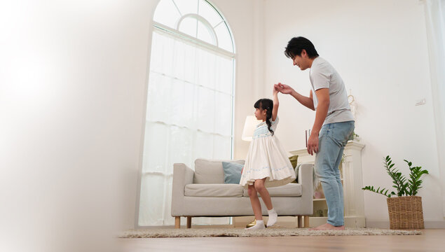 Asian father holding hands and dancing joyfully with his young daughter