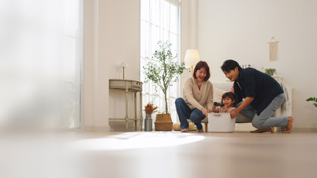 Multiracial parents playfully pushing daughter in a box at home