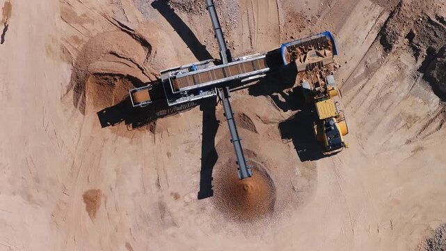 Aerial view of an open pit quarry shows a long conveyor, a blue feed hopper, and a yellow wheel loader loading. Conical sand and gravel piles form in strong sunlight.