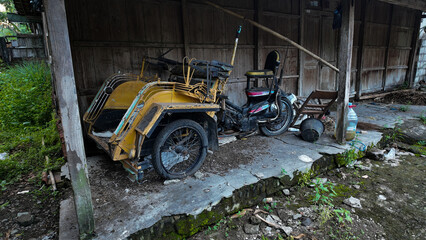 Fototapeta premium Abandoned yellow vehicle resting in rustic shed surrounded by greenery and concrete flooring