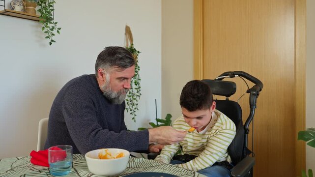 Caring father feeding disabled son in wheelchair at home