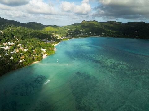 Aerial view of Anse A La Mouche bay with turquoise waters and lush green hills under a cloudy sky in Seychelles.