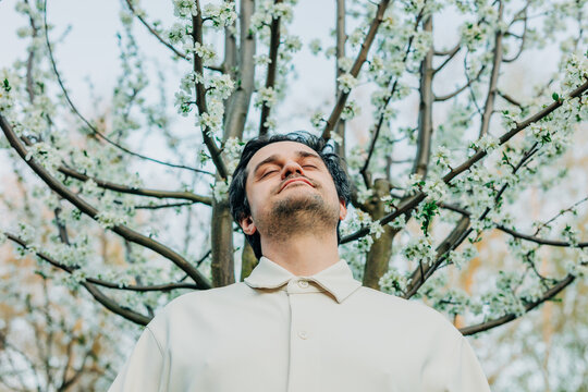 White European man in white shirt near blooming white tree enjoying spring allergy-free pollen