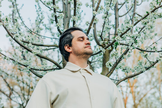 White European man in white shirt near blooming white tree enjoying spring allergy-free pollen