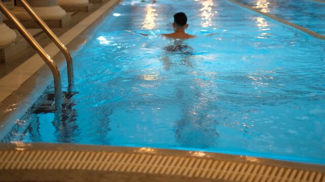 Young dark-haired man swimming in gym pool