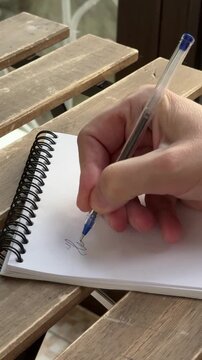 Close up video of a hand writing a friendly message in a spiral notebook with blue pen. Casual personal communication scene with handwritten greeting and note writing outdoors