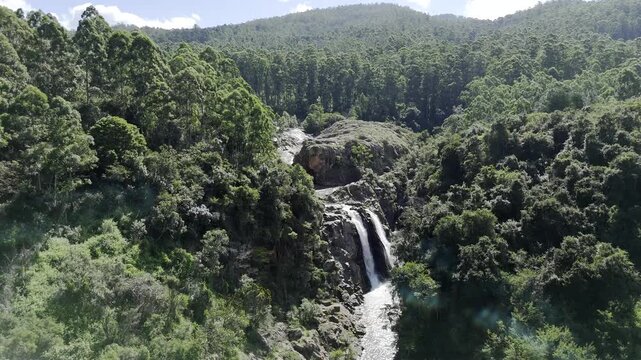 Drone lowers over Lusushwana River with view of Mantenga waterfall on a sunny day in Ezulwini, Eswatini