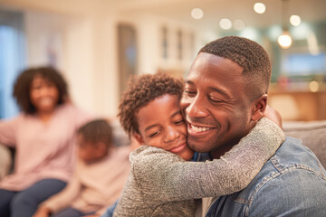 Fototapeta premium A father and son share a warm hug while smiling, with family members relaxing together in the cozy background at home.