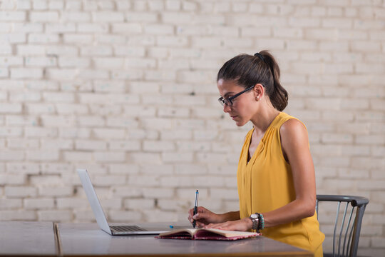 Young professional woman working on laptop and notebook in a creative coworking startup office space