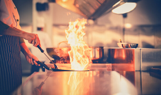 Chef in restaurant kitchen at stove and pan cooking flambe on food