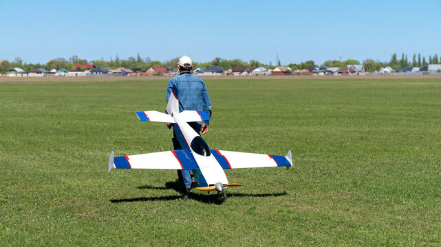 Man carrying a large RC model airplane on a green airfield