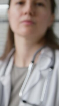 Vertical POV shot of young adult female GP reviewing eye condition of patient with penlight while testing pupil dilation during routine examination in healthcare office