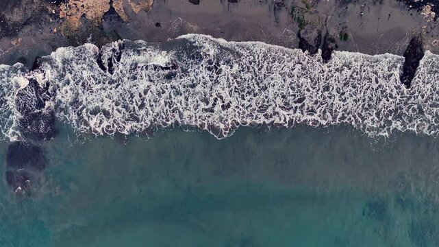 Aerial looking down at waves on a black sand beach in Bali Indonesia.