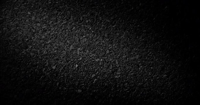 Black Gravel Texture. Slow Diagonal Panning. Extreme close-up of rough black granular surface with dramatic low key lighting.