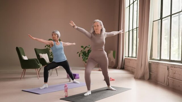 Two senior women in activewear practice warrior pose on mats, mindful yoga
