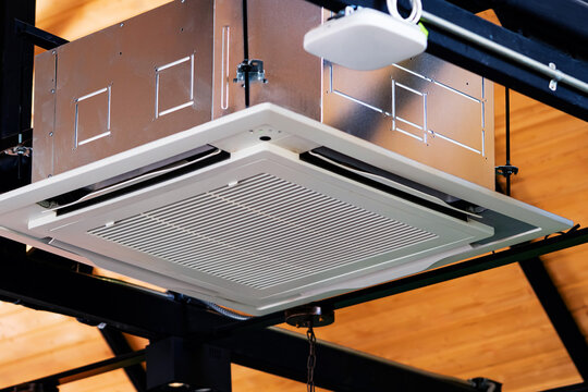 Modern cassette type air conditioner installed on loft ceiling with steel beams and wooden roof. Ceiling-mounted cassette air conditioning unit integrated into modern interior design. HVAC systems.