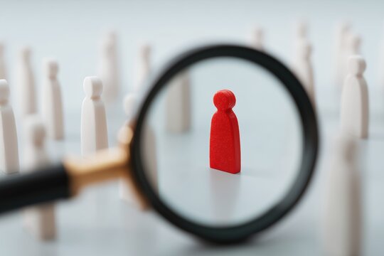 Focus and Insight: A unique red figure is meticulously scrutinized through a magnifying glass, suggesting keen observation and detailed analysis amidst many figures.