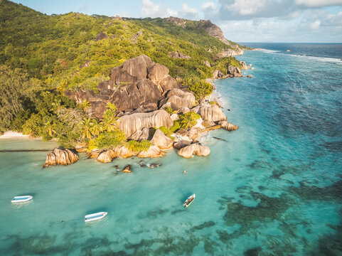 Aerial view of Anse Source d'Argent beach featuring iconic granite boulders, turquoise waters, and small boats near lush tropical hills in L'Union Estate, Seychelles.