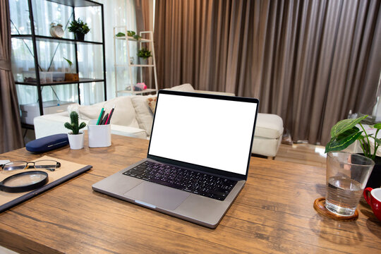laptop computer with blank white screen, with workspace and office supplies on a wooden desk