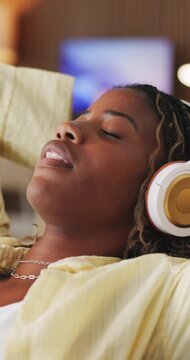 Relax, stretching and black woman with headphones on sofa, mindfulness audio guide and streaming music. Rest, listen and happy person with meditation track for stress relief, peace and tech in home
