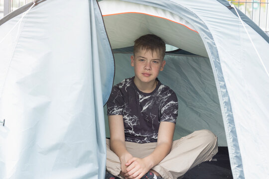 boy sitting in tent gray camping background boy resting inside a small tourist tent looking at camera with neutral expression outdoors on a summer day concept of tourism, recreation, lifestyle