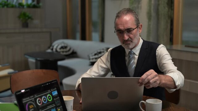 Focused senior business executive thinking deeply while analyzing corporate data on a laptop in a modern office. Mature entrepreneur solving complex problems and making strategic financial decisions.