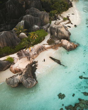 Aerial view of Anse Source d'Argent beach with its iconic granite boulders, white sand, and turquoise water with a person standing on the shore in L'Union Estate, Seychelles.