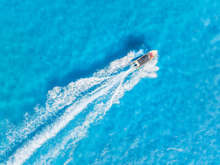 Obraz premium Aerial top down view of a speed boat cruising through turquoise sea waves. Summer vacation and travel concept. Drone shot of azure ocean water and white foam trail.