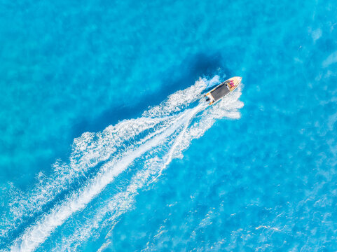 Aerial top down view of a speed boat cruising through turquoise sea waves. Summer vacation and travel concept. Drone shot of azure ocean water and white foam trail.