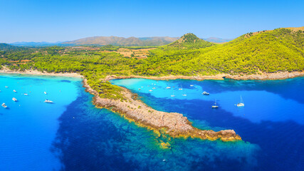Fototapeta premium Aerial view of Cala Agulla beach and turquoise bay with boats in Mallorca. Scenic Balearic Islands coastline landscape in Spain. Summer vacation and Mediterranean nature from drone.