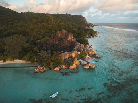 Aerial view of Anse Source d'Argent beach featuring iconic granite boulders, turquoise water, and a small boat during golden hour in L'Union Estate, Seychelles.