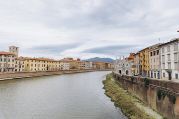 Fototapeta premium Arno river flowing through Pisa cityscape with Santa Maria della Spina and historic buildings in Tuscany, Italy