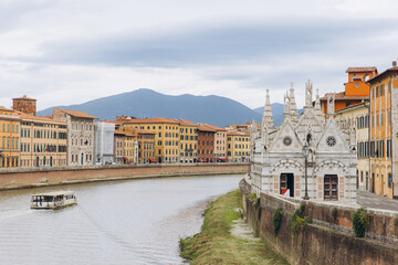 Fototapeta premium Arno river flowing through Pisa cityscape with Santa Maria della Spina church and historic riverside buildings